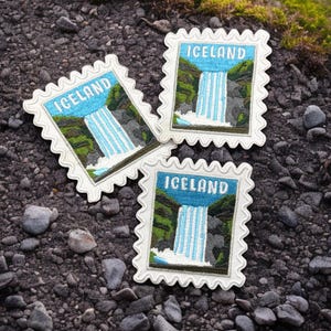 May include: Three rectangular embroidered patches with scalloped edges, each featuring a blue sky, a white waterfall, and green landscape with the word ICELAND in white capital letters, designed to resemble a postage stamp.