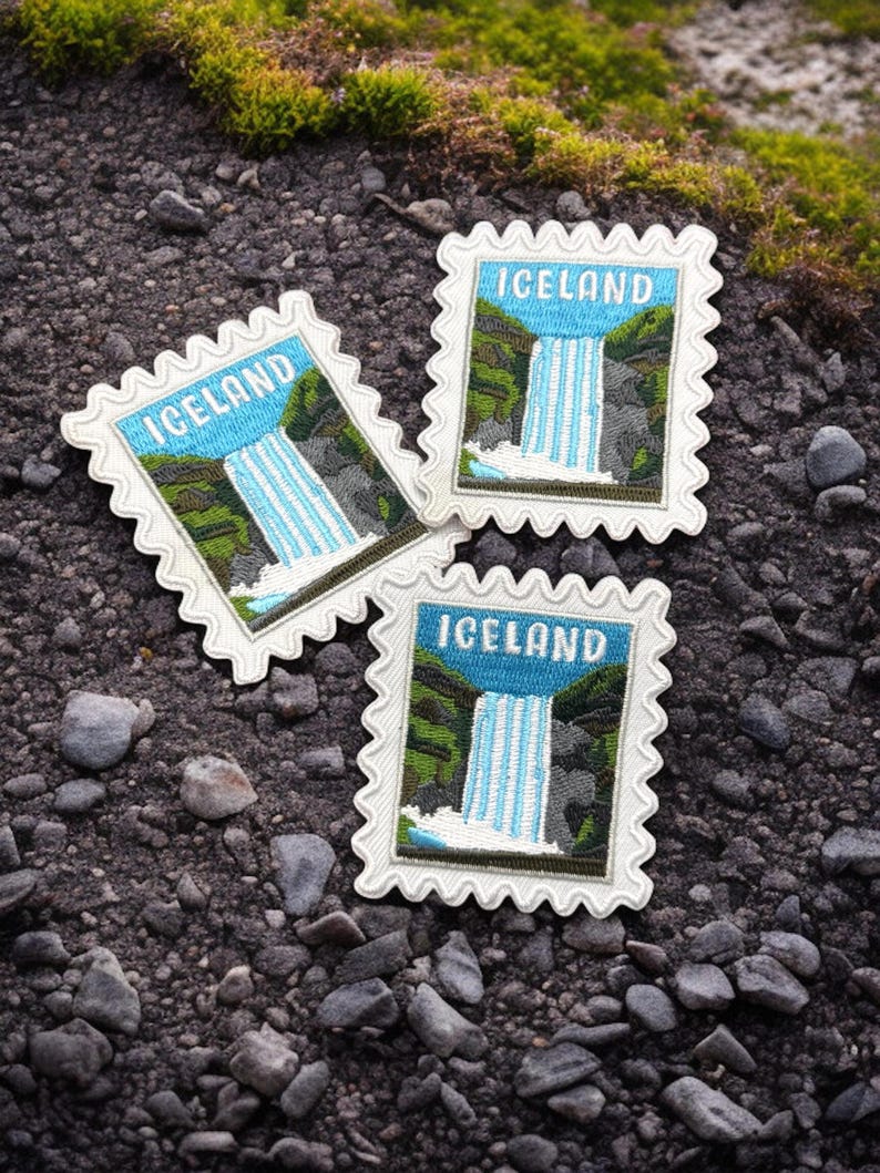 May include: Three rectangular embroidered patches with scalloped edges, each featuring a blue sky, a white waterfall, and green landscape with the word ICELAND in white capital letters, designed to resemble a postage stamp.
