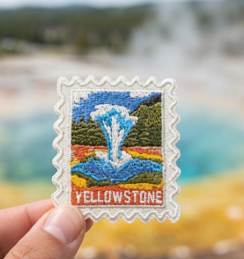 May include: A rectangular embroidered patch with a scalloped edge, featuring a colorful landscape scene of a geyser erupting. The design includes blue water, green trees, and orange ground, with the word YELLOWSTONE stitched in white at the bottom.