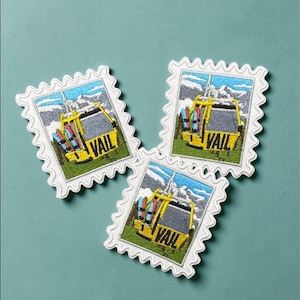 May include: Three embroidered patches in the shape of postage stamps. Each patch features a yellow ski lift with the word "VAIL" and a mountain scene. The patches have a white border with a scalloped edge. The background is a teal color.