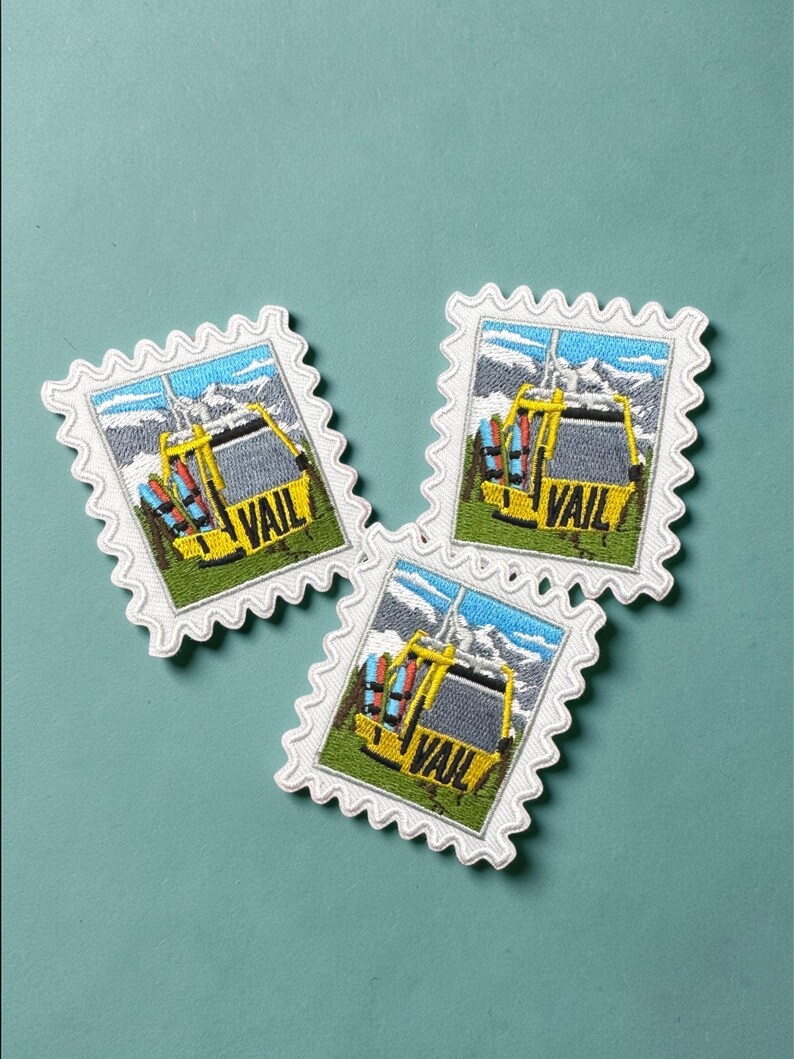 May include: Three embroidered patches in the shape of postage stamps. Each patch features a yellow ski lift with the word "VAIL" and a mountain scene. The patches have a white border with a scalloped edge. The background is a teal color.