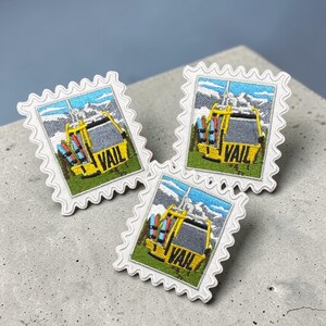 May include: Three embroidered patches in the shape of postage stamps. Each patch features a yellow ski lift with the word "VAIL" and a mountain scene. The patches have a white border with a scalloped edge.