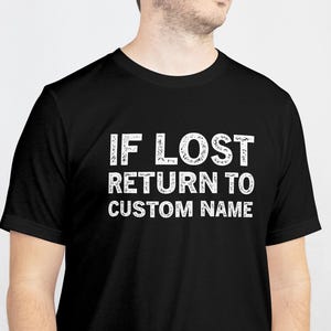 Könnte beinhalten: Schwarzes T-Shirt mit dem weißen Text "IF LOST RETURN TO CUSTOM NAME". Der Text ist fett und ohne Serifen. Das T-Shirt wird von einer Person getragen.