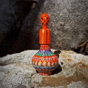 Pode incluir: Uma pequena garrafa laranja pintada à mão com um desenho floral. A garrafa tem uma tampa dourada e um padrão geométrico colorido no corpo.