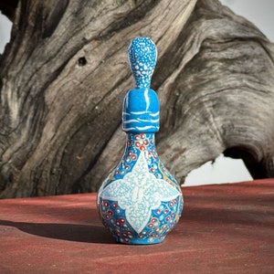 Pode incluir: Uma garrafa de cerâmica azul e branca com um design decorativo. A garrafa tem um corpo redondo e um pescoço longo e fino. O design apresenta pontos brancos, pontos vermelhos e uma forma de estrela branca.