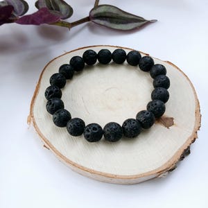 May include: A black lava rock beaded bracelet on a wooden surface.