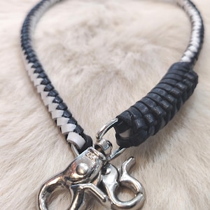May include: A braided lanyard featuring alternating black and white leather strands. The cord is finished with a thick black leather wrap near the base and includes a polished silver-tone metal swivel lobster clasp with a smaller attached hook.