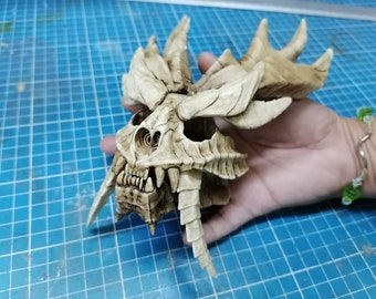 May include: A detailed, beige-colored sculpture of a horned skull with sharp teeth and intricate carvings. The skull has large, curved horns and a segmented lower jaw, suggesting a fantasy or mythological theme.