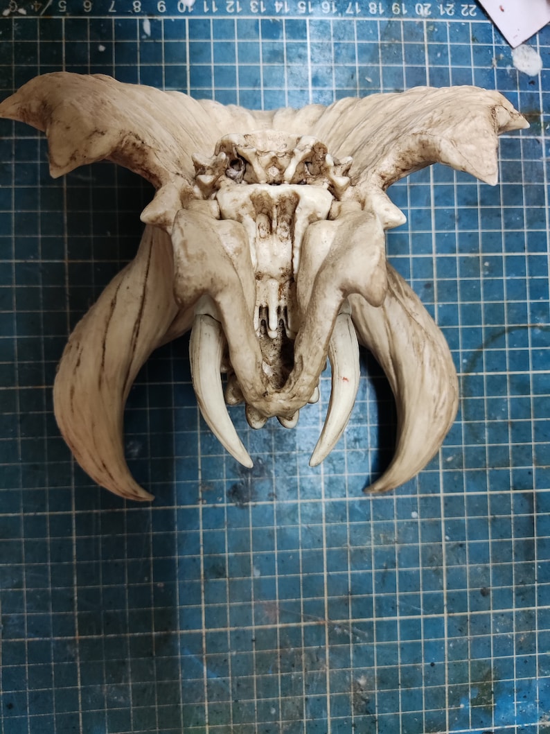 Puede incluir: Una escultura esquel&eacute;tica blanca y detallada de una criatura con grandes dientes puntiagudos y cuernos. La escultura est&aacute; hecha de un material texturizado y tiene un aspecto desgastado.