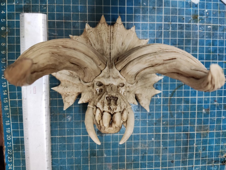 Puede incluir: Un cr&aacute;neo de cer&aacute;mica blanca con grandes cuernos, que se asemeja a un dinosaurio o una criatura m&iacute;tica. El cr&aacute;neo tiene dientes detallados y una superficie texturizada.