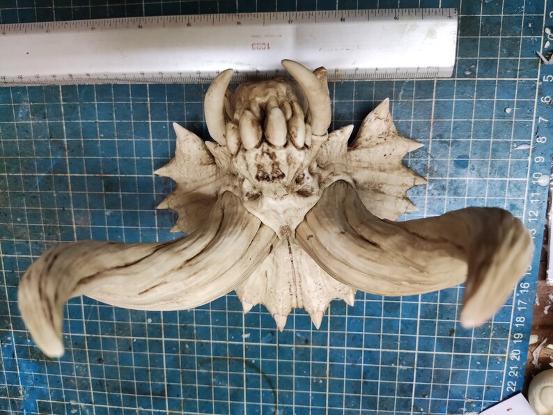 Puede incluir: Un cr&aacute;neo de cer&aacute;mica blanca con grandes cuernos, que se asemeja a una criatura m&iacute;tica. El cr&aacute;neo tiene un dise&ntilde;o detallado con dientes afilados y una superficie texturizada.