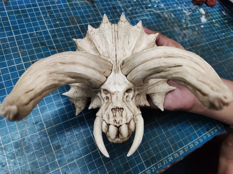 Puede incluir: Un cr&aacute;neo de cer&aacute;mica blanca con cuernos grandes y dientes afilados. El cr&aacute;neo est&aacute; detallado con caracter&iacute;sticas texturizadas que se asemejan a los huesos.