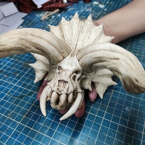 Puede incluir: Un cr&aacute;neo blanco, esculpido y detallado con grandes cuernos y dientes afilados. El cr&aacute;neo est&aacute; hecho de un material liso y texturizado y tiene un aspecto realista.