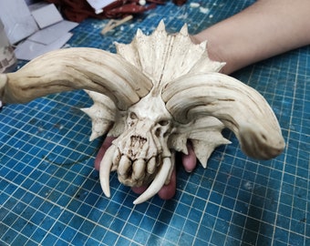 May include: A white, detailed, sculpted skull with large horns and sharp teeth. The skull is made of a smooth, textured material and has a realistic appearance.