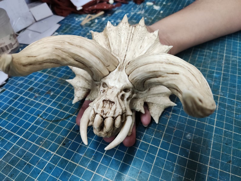 Puede incluir: Un cr&aacute;neo blanco, esculpido y detallado con grandes cuernos y dientes afilados. El cr&aacute;neo est&aacute; hecho de un material liso y texturizado y tiene un aspecto realista.