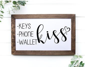 May include: A framed wooden sign with the text "Keys, Phone, Wallet, kiss" in black lettering. The word "kiss" is in cursive with a small heart at the end.
