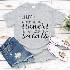 May include: A gray t-shirt with the text "CHURCH: A HOSPITAL FOR SINNERS NOT A MUSEUM FOR SAINTS" printed in black.