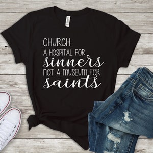 May include: Black t-shirt with white text that reads "Church: A hospital for sinners not a museum for saints."