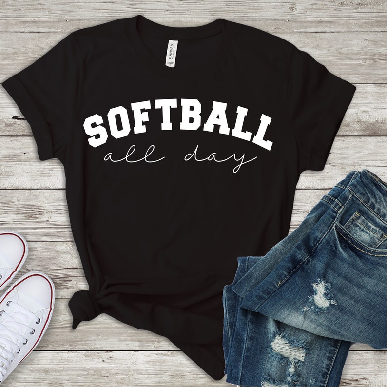 Op de afbeelding: Zwart T-shirt met witte tekst die "Softball all day" zegt in een lettertype in varsity-stijl.