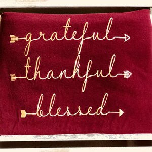 May include: Burgundy colored sweatshirt with gold lettering that reads "grateful", "thankful", and "blessed" with arrows on either side of each word.
