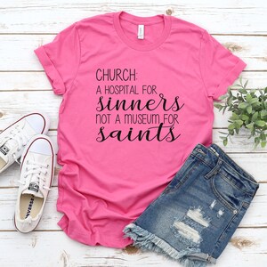 May include: Pink t-shirt with black text that reads "CHURCH: A HOSPITAL FOR SINNERS NOT A MUSEUM FOR SAINTS".