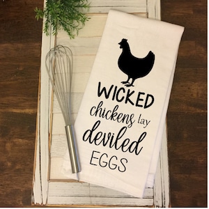 Pode incluir: Toalha de cozinha branca com uma silhueta preta de um frango e o texto "WICKED chickens lay deviled EGGS".