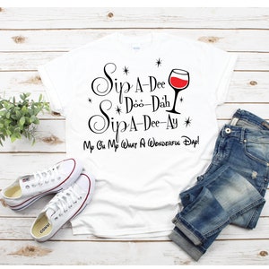 May include: White t-shirt with black text that reads "Sip A-Dee Doo-Dah Sip A-Dee-Ay" with a wine glass graphic and the text "My Oh My What A Wonderful Day!"