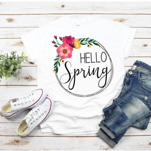 May include: White t-shirt with a floral wreath and the text "HELLO Spring" in black script.