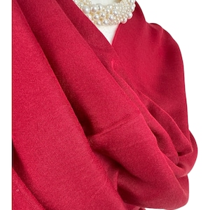 May include: A deep red, soft, and drapey scarf made of a fine knit fabric. The scarf is folded and draped over a mannequin's neck, with a pearl necklace on top.