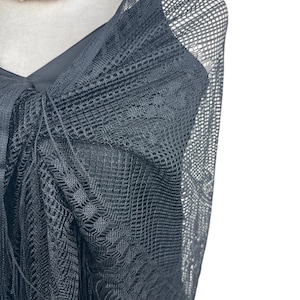 May include: A black sheer shawl with a delicate, intricate pattern and fringe detailing. The shawl is draped over a mannequin's shoulders.