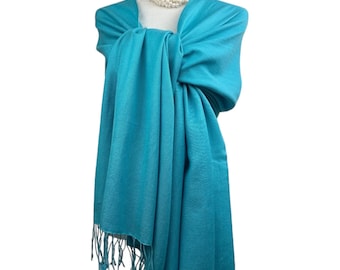May include: A turquoise blue pashmina shawl with fringe. The shawl is draped over a mannequin wearing a pearl necklace.