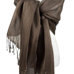 Pode incluir: Um len&ccedil;o retangular castanho-escuro s&oacute;lido com uma textura leve e transparente, apresentando detalhes de franjas delicadas nas bordas. O len&ccedil;o est&aacute; drapeado sobre um manequim branco, que tamb&eacute;m ostenta um colar de p&eacute;rolas brancas de v&aacute;rias voltas.