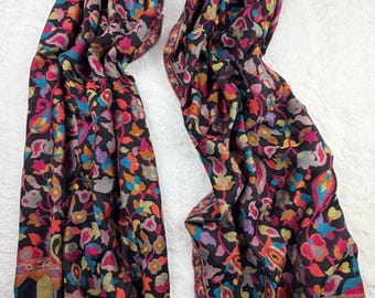 Pode incluir: Um cachecol preto com um padrão floral e paisley multicolorido e vibrante em toda a superfície. As extremidades do cachecol apresentam uma borda distinta com listras verticais em tons de azul, dourado e preto, com acabamento em franjas.