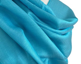 May include: A turquoise blue silk scarf draped over a mannequin. The scarf is soft and flowing, with a subtle sheen.