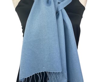 May include: A light blue pashmina scarf with a fringe border. The scarf is draped around a mannequin's neck and tied in a loose knot.