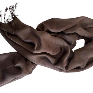 Pode incluir: Um cachecol castanho-escuro s&oacute;lido com uma textura suave e ligeiramente transl&uacute;cida, com franjas delicadas em ambas as extremidades. O tecido est&aacute; drapeado em dobras soltas e fluidas, criando uma apar&ecirc;ncia suave e leve com uma cor castanha uniforme.