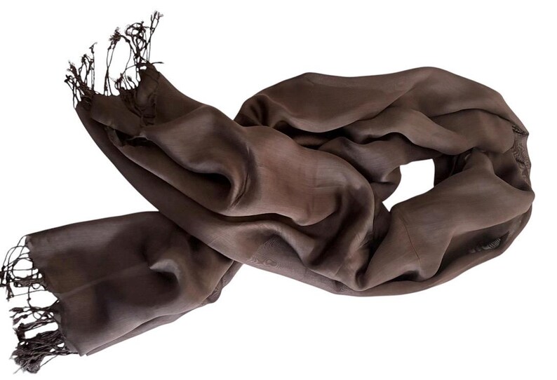 Pode incluir: Um cachecol castanho-escuro s&oacute;lido com uma textura suave e ligeiramente transl&uacute;cida, com franjas delicadas em ambas as extremidades. O tecido est&aacute; drapeado em dobras soltas e fluidas, criando uma apar&ecirc;ncia suave e leve com uma cor castanha uniforme.