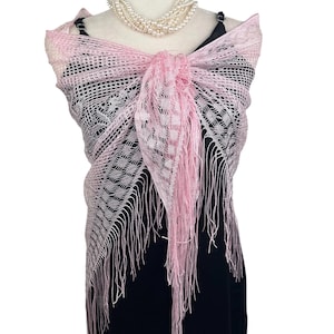 May include: A pink lace shawl with fringe trim. The shawl is draped over a mannequin wearing a black dress and a pearl necklace.