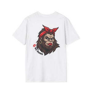 Peut inclure: T-shirt blanc avec une illustration de dessin animé d'un personnage ressemblant à Bigfoot, portant un bandana rouge, une boucle d'oreille dorée et du rouge à lèvres rouge. Le texte "Big Momma" et une marque de baiser rouge sont également sur le t-shirt.