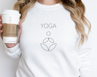 Może przedstawiać: Biała bluza z napisem "YOGA" i stylizowanym symbolem jogi w kolorze czarnym.