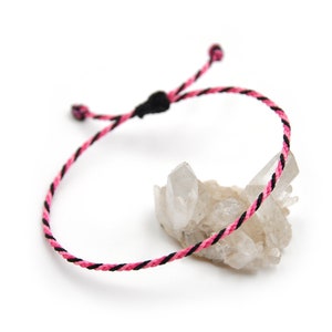 May include: A pink and black braided cord bracelet with adjustable sliding knots.