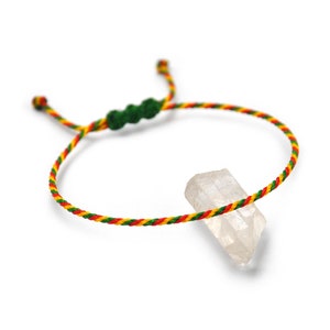 Op de afbeelding: Handgemaakte armband met een helder kwartskristal en een gevlochten koord in rood, geel en groen. De verstelbare armband heeft een schuifknoopsluiting en groene kralen.