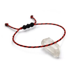 Peut inclure: Un bracelet en cordon tressé rouge et noir avec un pendentif en cristal de quartz transparent.