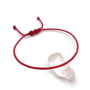 Peut inclure: Un bracelet en fil rouge avec un pendentif en cristal de quartz clair. Le bracelet est réglable et comporte une fermeture à nœud coulissant. Le cristal est de forme naturelle et brute.