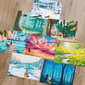 Peut inclure: Plusieurs impressions d'art paysagères représentant diverses scènes, notamment une forêt, une maison, un coucher de soleil et une rivière enneigée. Chaque impression présente un environnement unique avec des couleurs vives et des illustrations détaillées. Les impressions sont disposées sur une surface en bois.