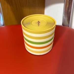 May include: A set of yellow, green, orange, and white striped stacking cups. The cups are made of plastic and have a smooth, rounded surface. The cups are stacked on top of each other, with the largest cup at the bottom and the smallest cup at the top.
