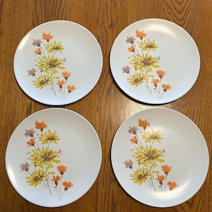 May include: Set of four white ceramic dinner plates with a floral design. The flowers are yellow, orange, and brown.
