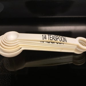 May include: A set of five white measuring spoons, nested together. The largest spoon is labeled "1/4 Teaspoon".