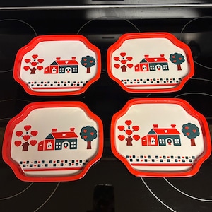 May include: Set of four decorative trays with a red border and a white interior. Each tray features a house, heart-shaped trees, and a regular tree design in red, blue, and green.