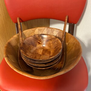 Pu&ograve; includere: Un set di insalatiere e utensili da servizio in legno. Le insalatiere sono impilate all'interno di una ciotola pi&ugrave; grande, e gli utensili sono posizionati sopra le insalatiere. Le insalatiere sono realizzate in legno marrone chiaro e hanno un motivo intrecciato.